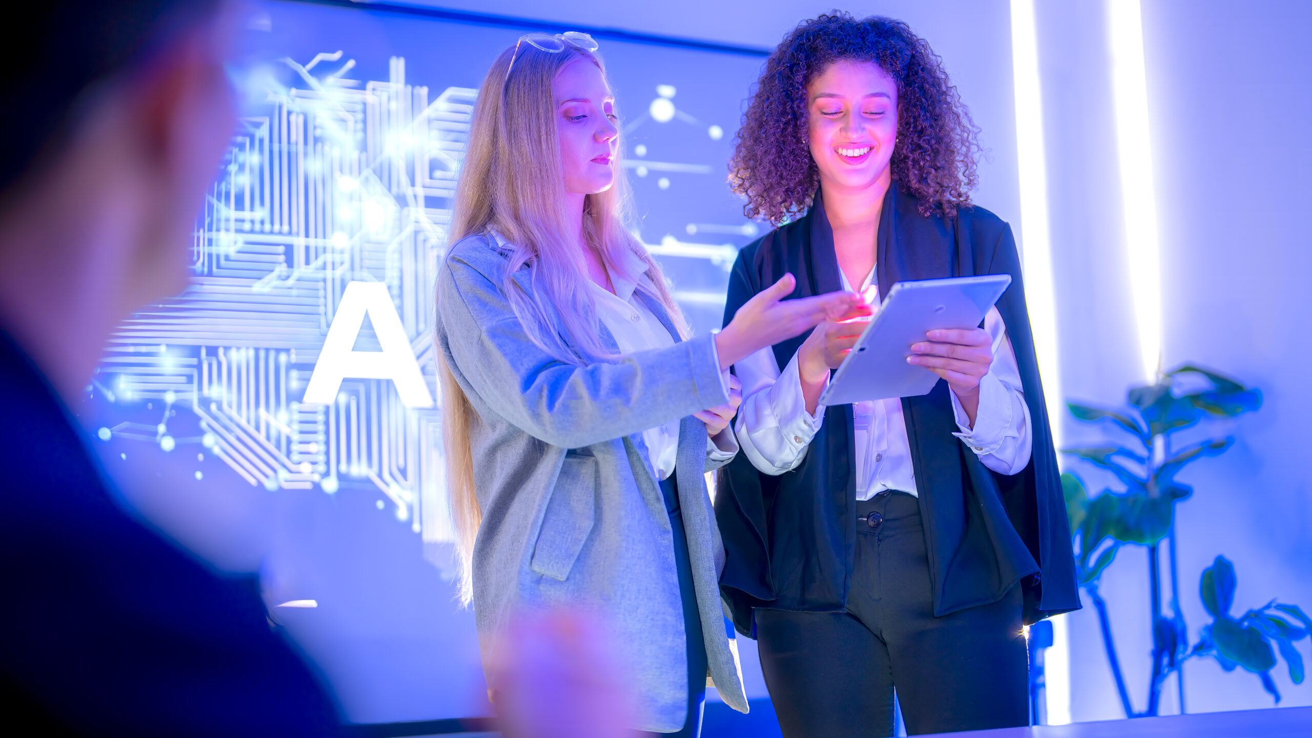Two business professionals collaborating with a digital tablet in front of an AI-themed display, representing artificial intelligence and marketing automation.