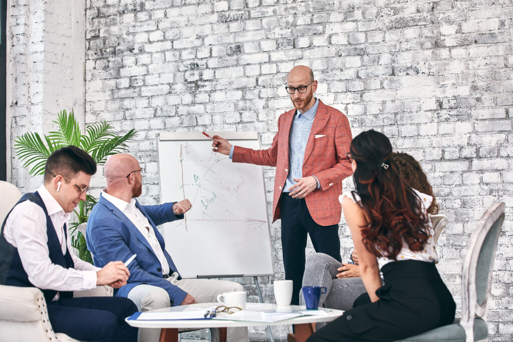 Business leader presenting charts on a whiteboard while coaching a team of professionals during a collaborative meeting.